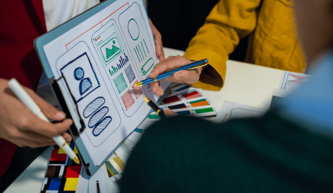 Team collaborating on UI design, using pen and paper wireframes. - International Awards