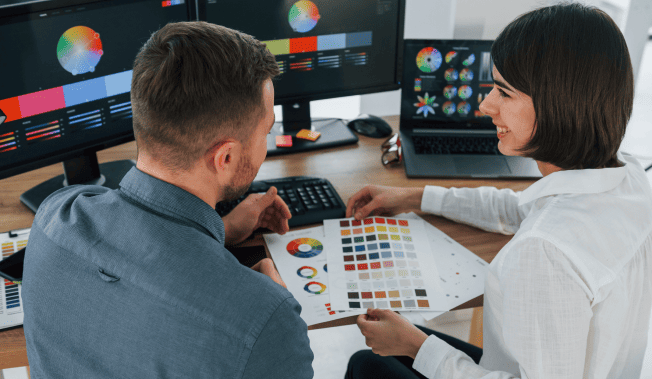 Two designers review color palettes on computer screens and printed samples. - International Awards