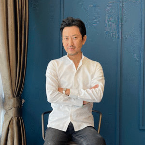 So Iizuka, a man in a white shirt, sits with arms crossed. - International Awards