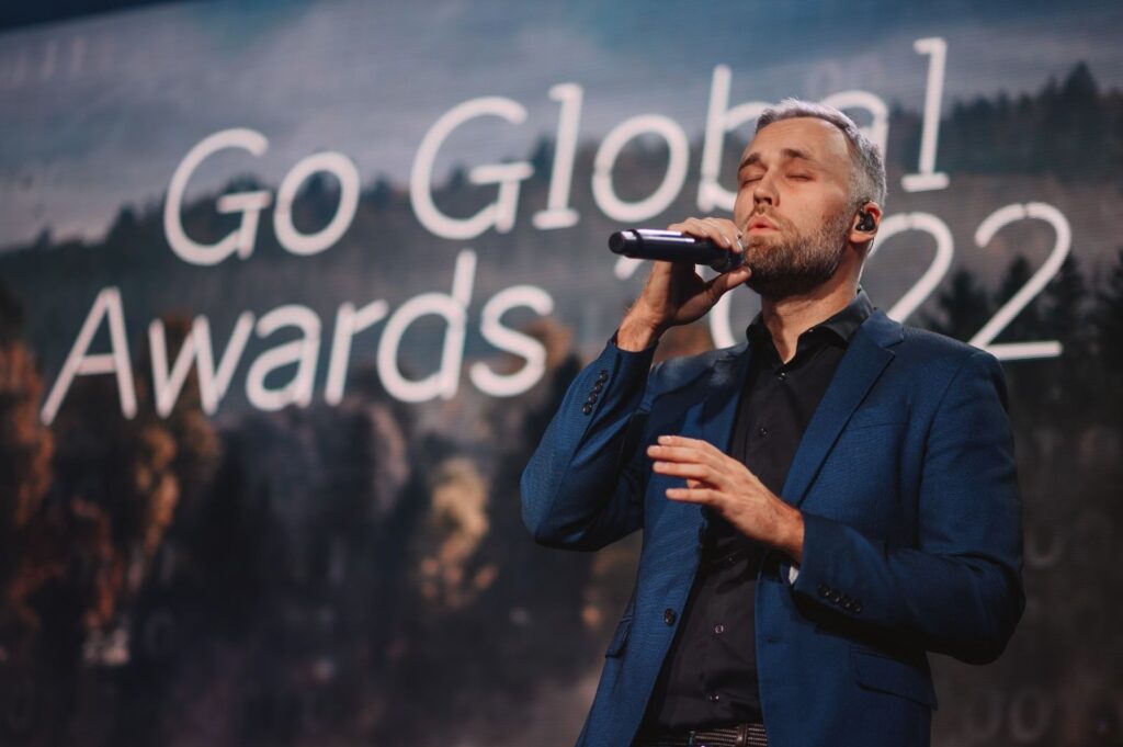 Man in blue suit singing into microphone at Go Global Awards 2022. - International Awards